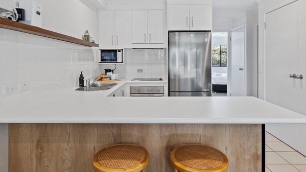 Une cuisine moderne avec des meubles blancs, un réfrigérateur en acier inoxydable, un four à micro-ondes et un îlot central en bois équipé de deux tabourets.
