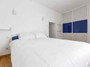 Un dormitorio moderno con una cama grande, paredes blancas y un armario con detalles azules.