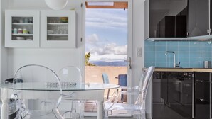 A modern kitchen with a view of the mountains, a dining area with clear chairs, and a blue tiled backsplash. - Opuntia Location en Méditerranée (Escales)