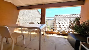 Un balcón con mesa y sillas, plantas en macetas y vista panorámica de la ciudad.