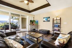 Relax in this spacious living room with a panoramic view of the surrounding landscape, featuring a leather sofa, coffee table, and television.