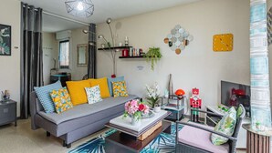 Un salon moderne avec un canapé gris, des coussins colorés, une table basse et un fauteuil en osier.