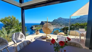 Ein Balkon mit Meerblick, ein Korbstuhl und ein Tisch mit Rosen.