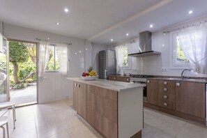A modern kitchen with a central island, wooden cabinets, and a stainless steel range hood. - House on the beachfront with 4 bedrooms, 2 bathrooms and barbecue (Alcúdia)