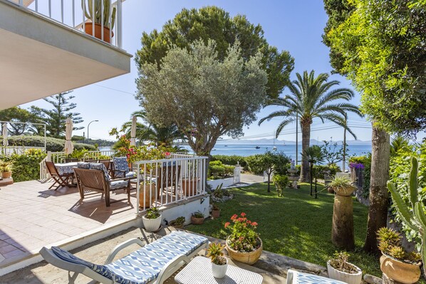 A patio with outdoor furniture, a large tree, and a view of the sea.