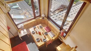 Un comedor acogedor con una mesa lista para cuatro personas, ventanas grandes y vistas al tejado.