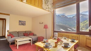 Una sala de estar acogedora con un sofá, una mesa de comedor dispuesta para el té y un ventanal con vistas a la montaña.
