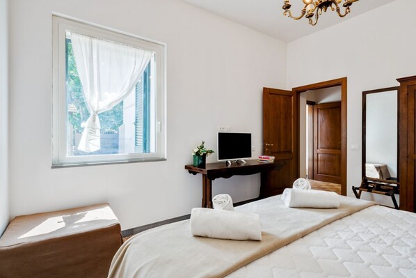 A hotel room with a bed, a desk, a television, a window with curtains, and a mirror.