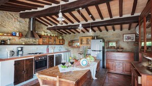 A rustic kitchen with wooden cabinets, a stone wall, and a wooden ceiling. - Elks Tower (Toscana)