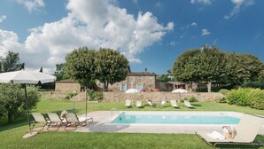 A pool area with lounge chairs and umbrellas, surrounded by a stone wall and trees. - Elks Tower (Toscana)