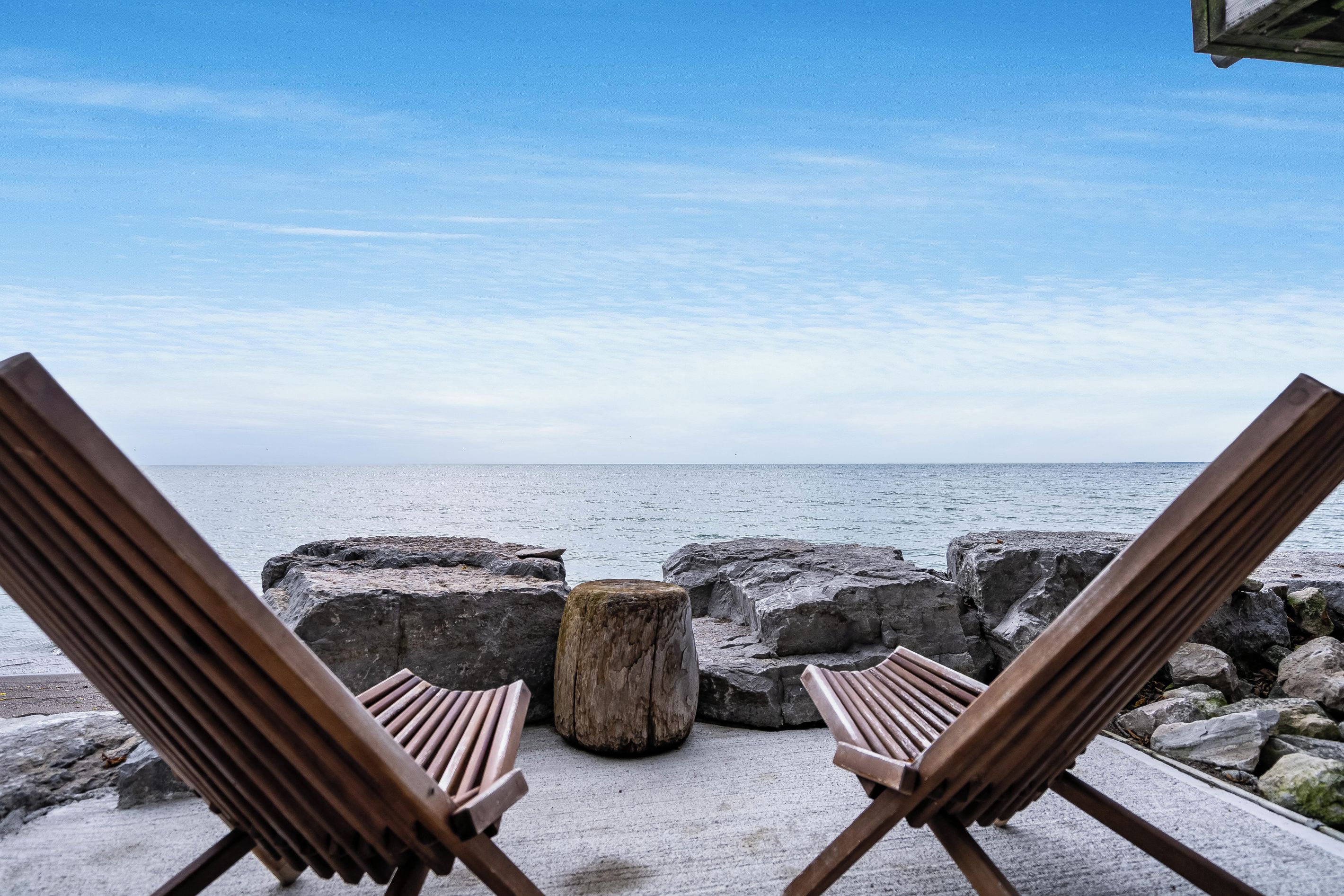 Two wooden lounge chairs facing a rocky shoreline with a view of the sea.