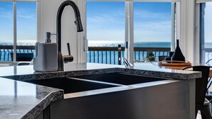 A modern kitchen with a large island, dark cabinetry, and a view of the ocean through large windows.