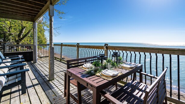 A wooden deck with a table set for dining, overlooking a body of water.