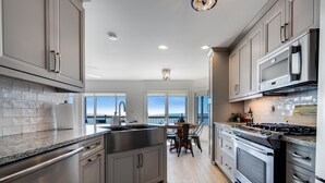 A modern kitchen with stainless steel appliances, grey cabinetry, and a view of the ocean. - Lakefront w/ Hot Tub + Private Beach | Near Point Pelee (Leamington)
