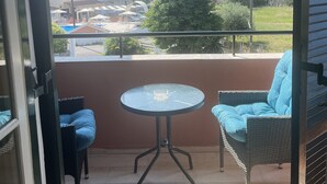 Un balcón con una mesa de vidrio y dos sillas de mimbre, con vistas a una zona residencial con edificios y una palmera.