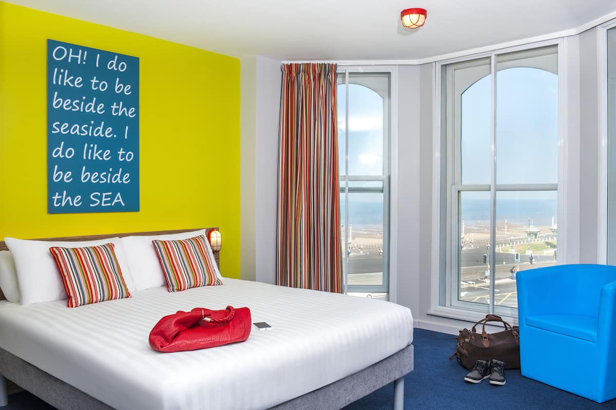 A hotel room with a large bed, a view of the airport, and a bright yellow wall.