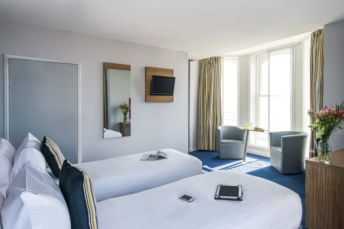 A hotel room with two beds, a TV, a chair, and a desk.