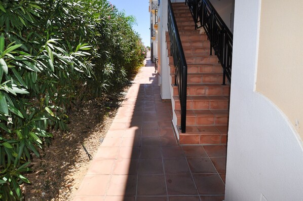 A narrow pathway leading to a staircase with a black railing, flanked by dense green foliage on one side and a building on the other. - Apt. Oura Sea View OCV - Close to Oura beach (Albufeira)