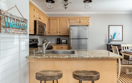A kitchen with wooden cabinets, a stainless steel refrigerator, granite countertops, and two bar stools.