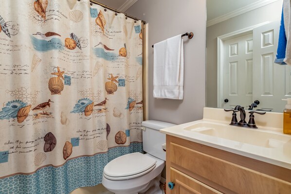 A bathroom with a white toilet, a beige sink, and a shower curtain with sea creature designs.