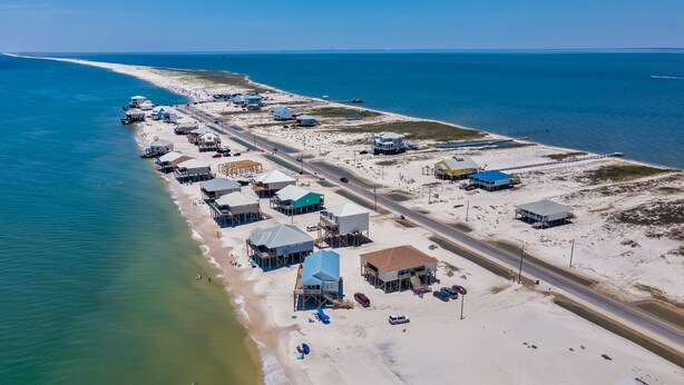 Luftaufnahme einer Küstenregion mit Gebäuden, einer Straße und einem Strand.