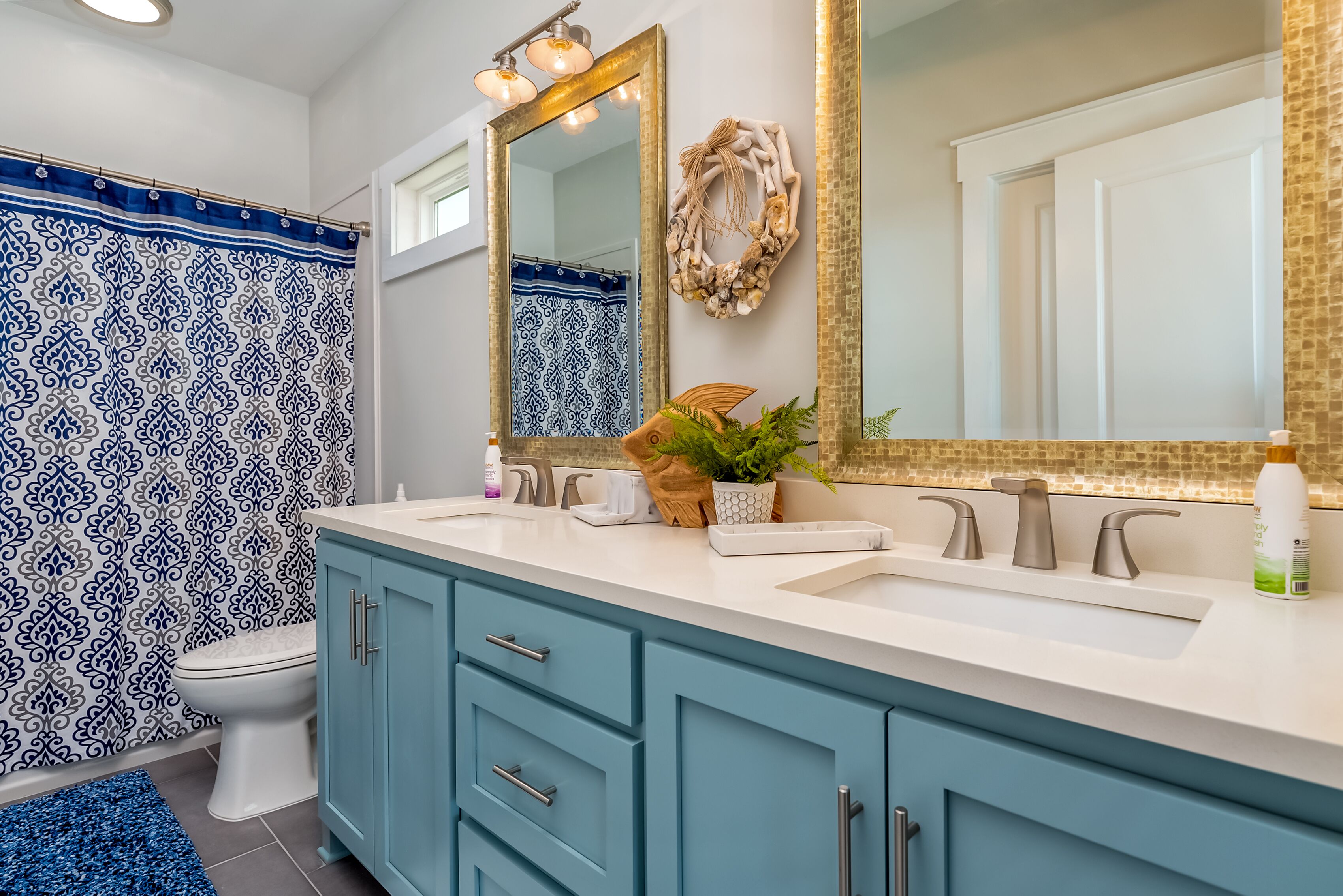 A bathroom with a white sink, two faucets, a mirror with a gold frame, and a blue vanity.