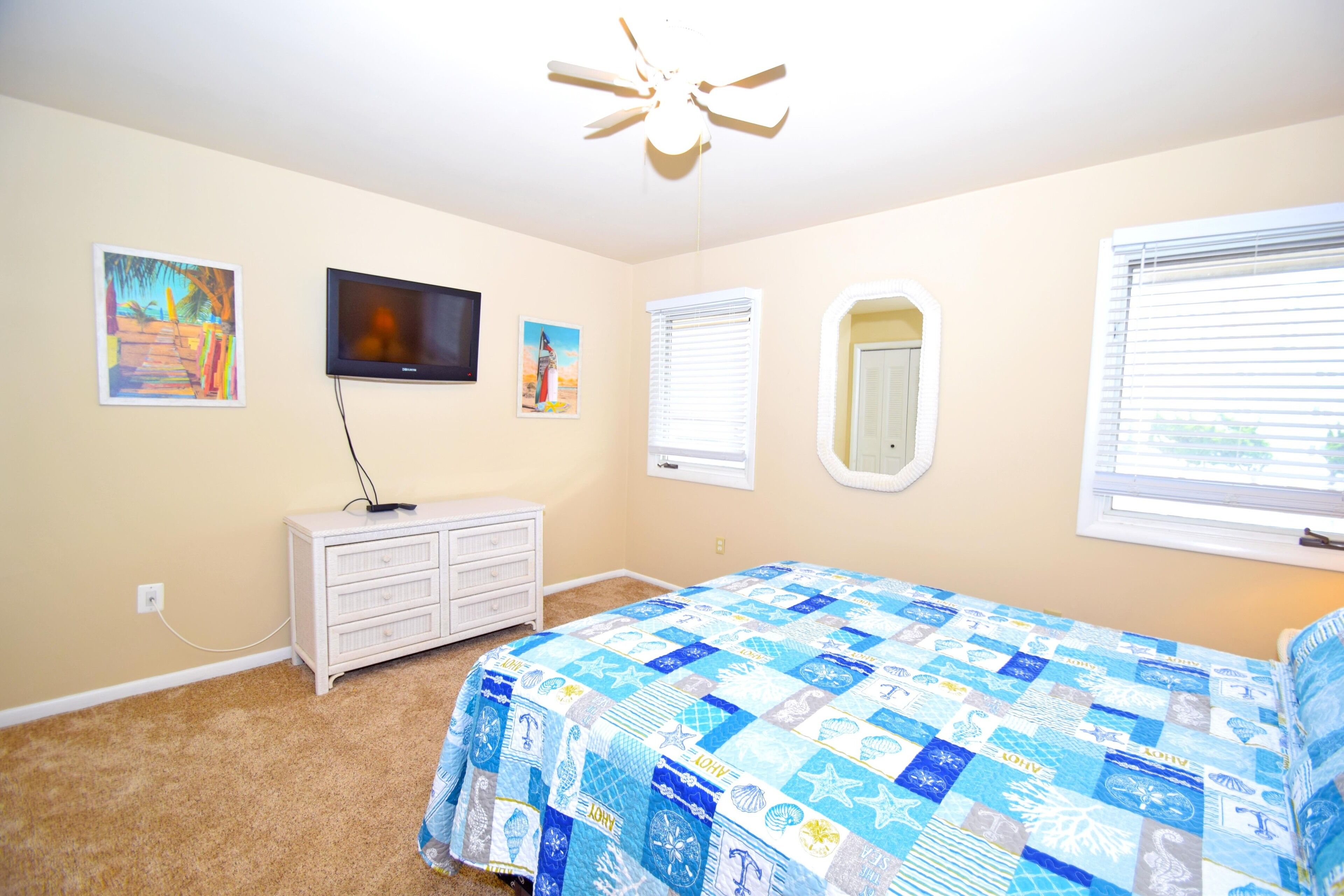 Une chambre à coucher avec un grand lit, une télévision, une commode et un ventilateur de plafond.