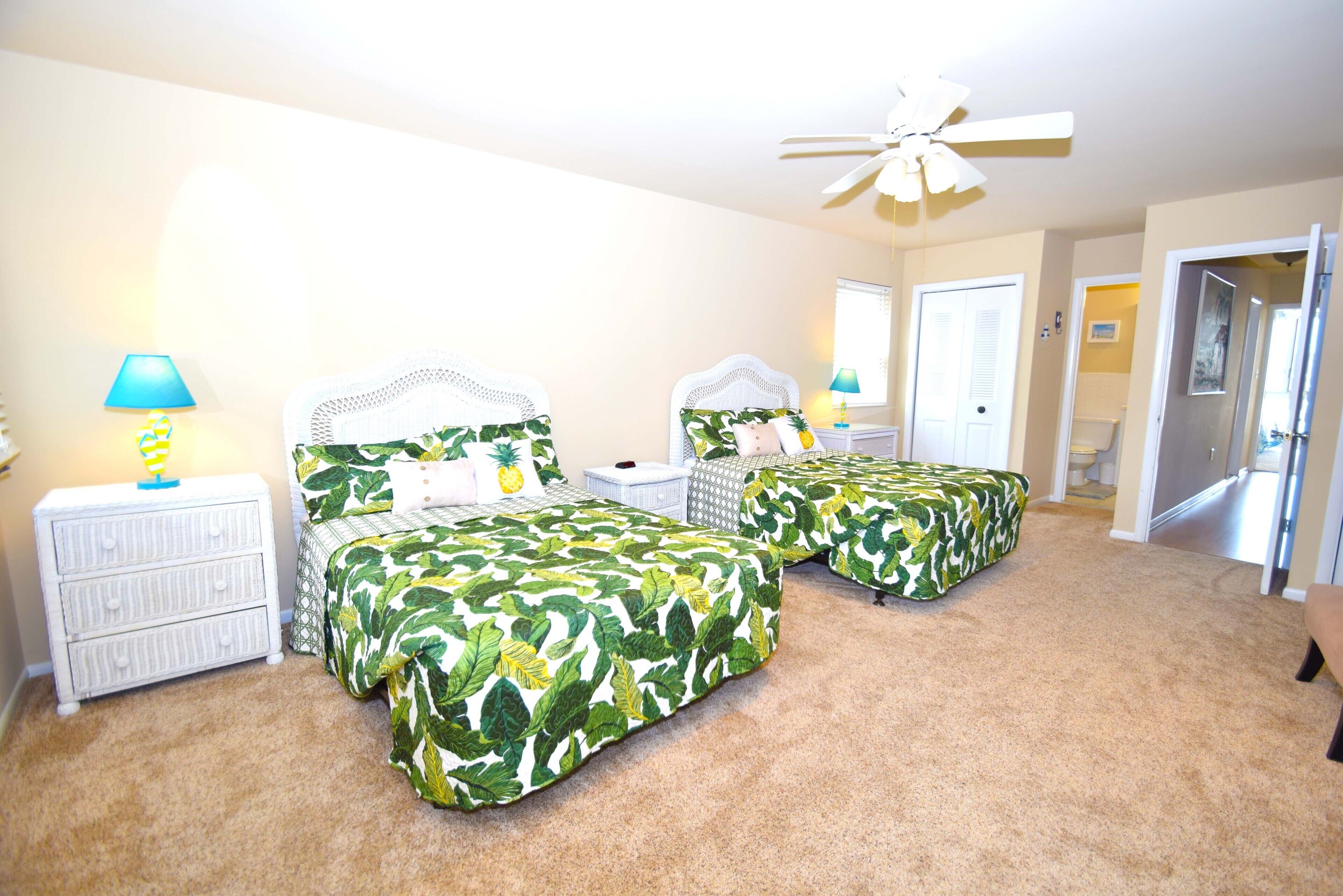 A bedroom with two beds, a ceiling fan, and a nightstand with a lamp.