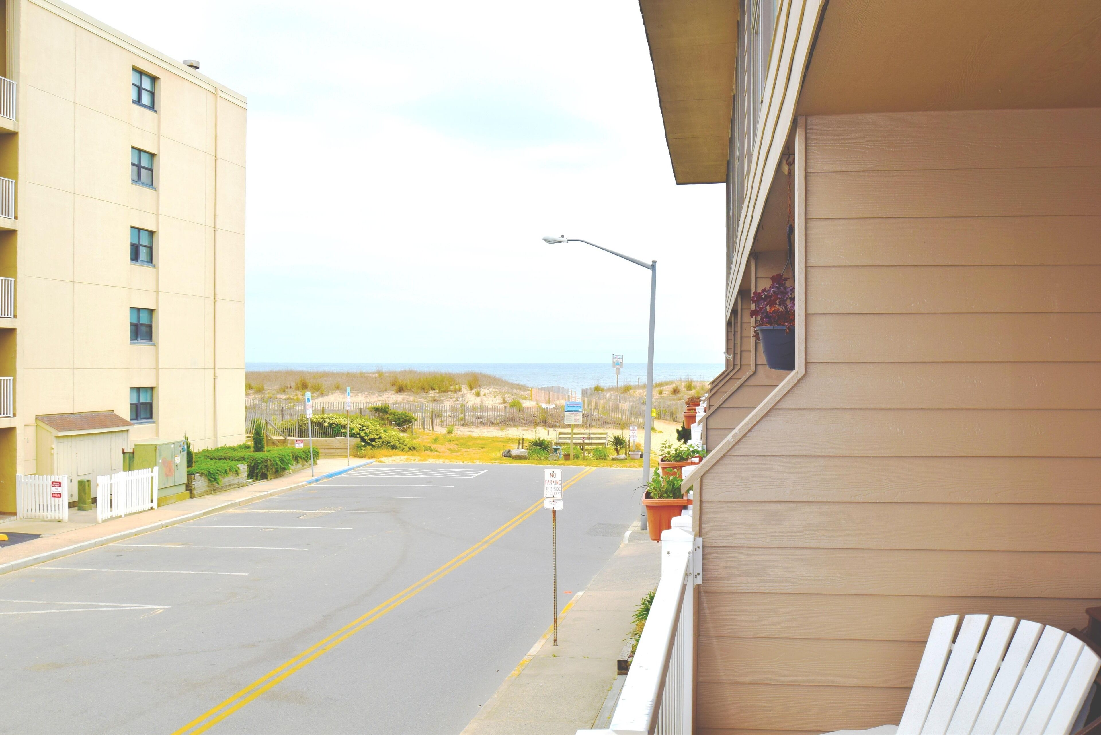 A view from a balcony overlooking a street with a building on the left and a clear sky.