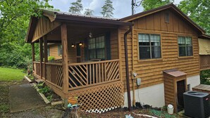 Une cabane en bois avec une véranda, une petite terrasse et un grand climatiseur.