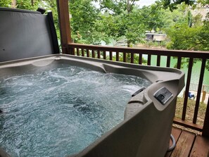 A hot tub on a wooden deck with a view of a green landscape and a building in the background.