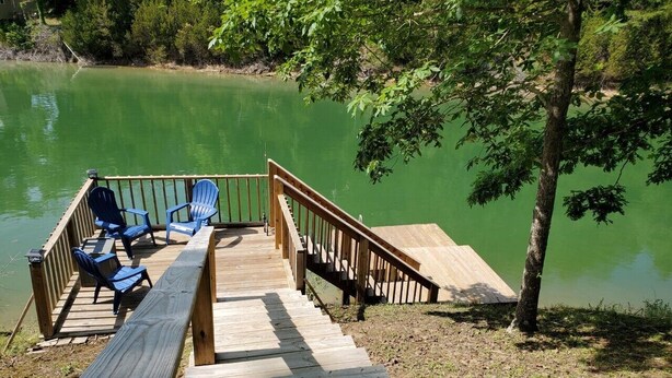Une jetée en bois, avec des chaises bleues et une rambarde menant à un lac vert et paisible.