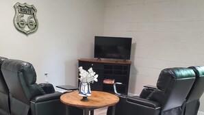 Un salon comprenant deux fauteuils inclinables en cuir noir, une table basse en bois, un téléviseur fixé au mur et une cheminée.