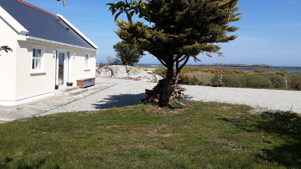 A house with a gravel driveway, a tree in the front yard, and a view of the sea in the background. - Seaside Cottage in Renvyle (Connemara)
