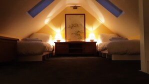 A cozy attic bedroom with two beds, a central nightstand, and a framed picture on the wall. - Seaside Cottage in Renvyle (Connemara)