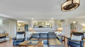 A modern living room with a leather sofa, a wooden coffee table, and a dining area with a kitchen in the background. - Beautiful views of Little Traverse Bay and a spacious wraparound deck (Petoskey)