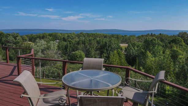 A deck with a glass table and wicker chairs, overlooking a forest and a distant view of mountains. - Beautiful views of Little Traverse Bay and a spacious wraparound deck (Petoskey)