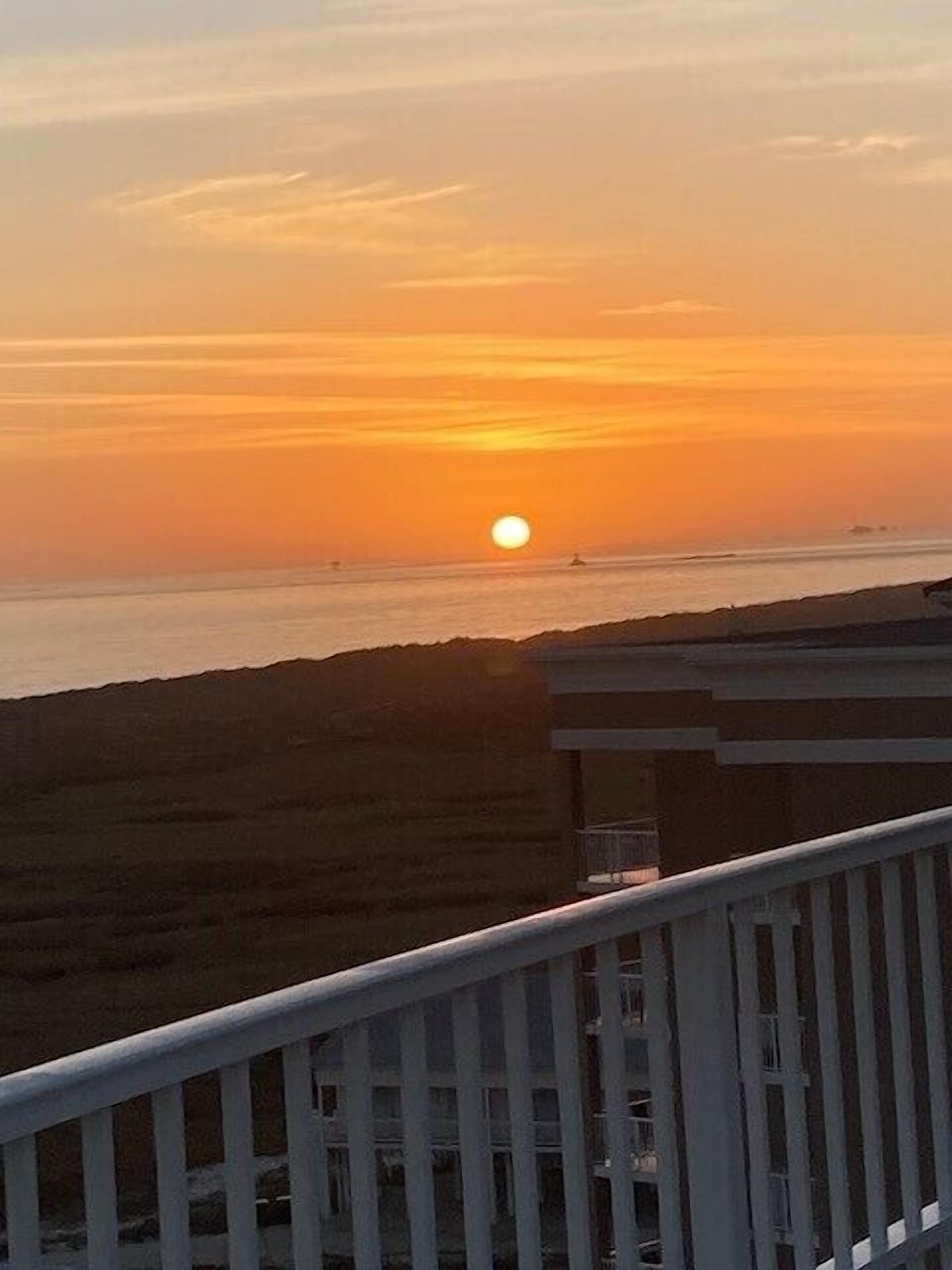 Ein Sonnenuntergang über dem Meer mit einem Gebäude im Vordergrund.