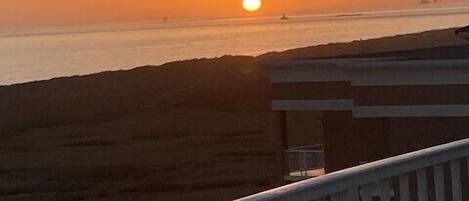 Ein Sonnenuntergang über dem Meer mit einem Gebäude im Vordergrund.