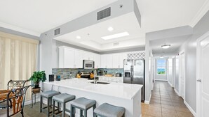 Une cuisine moderne avec des meubles blancs, un îlot central doté de tabourets de bar et une vue sur l’océan par une fenêtre.