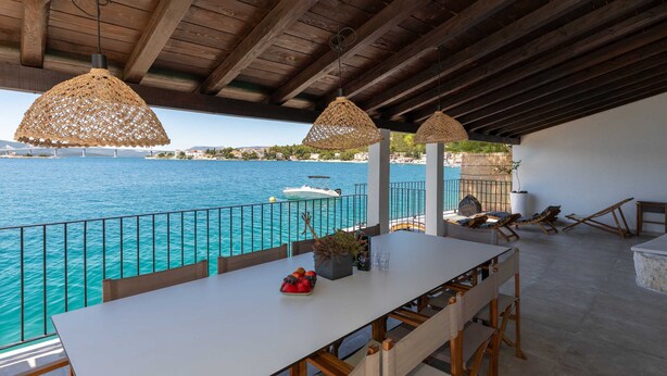 Ein Essbereich im Freien mit Blick auf das Meer, einem weißen Tisch und Körbchenpendelleuchten.