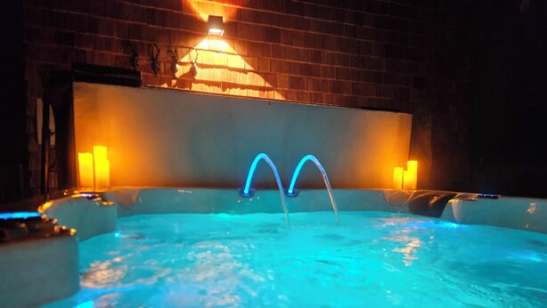 Ein Whirlpool mit zwei blauen Düsen, umgeben von Kerzen, in einem schwach beleuchteten Raum mit Backsteinwänden.