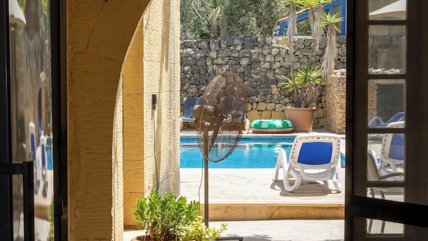 An entrance to a pool area with a stone wall, a potted plant, and a chair. - Gozo Holiday Farmhouse Accommodation (Gharb Gozo)