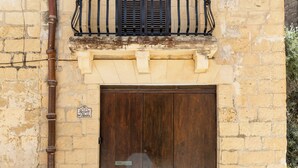 A stone building with a wooden door and a small balcony with a metal railing. - Gozo Holiday Farmhouse Accommodation (Gharb Gozo)