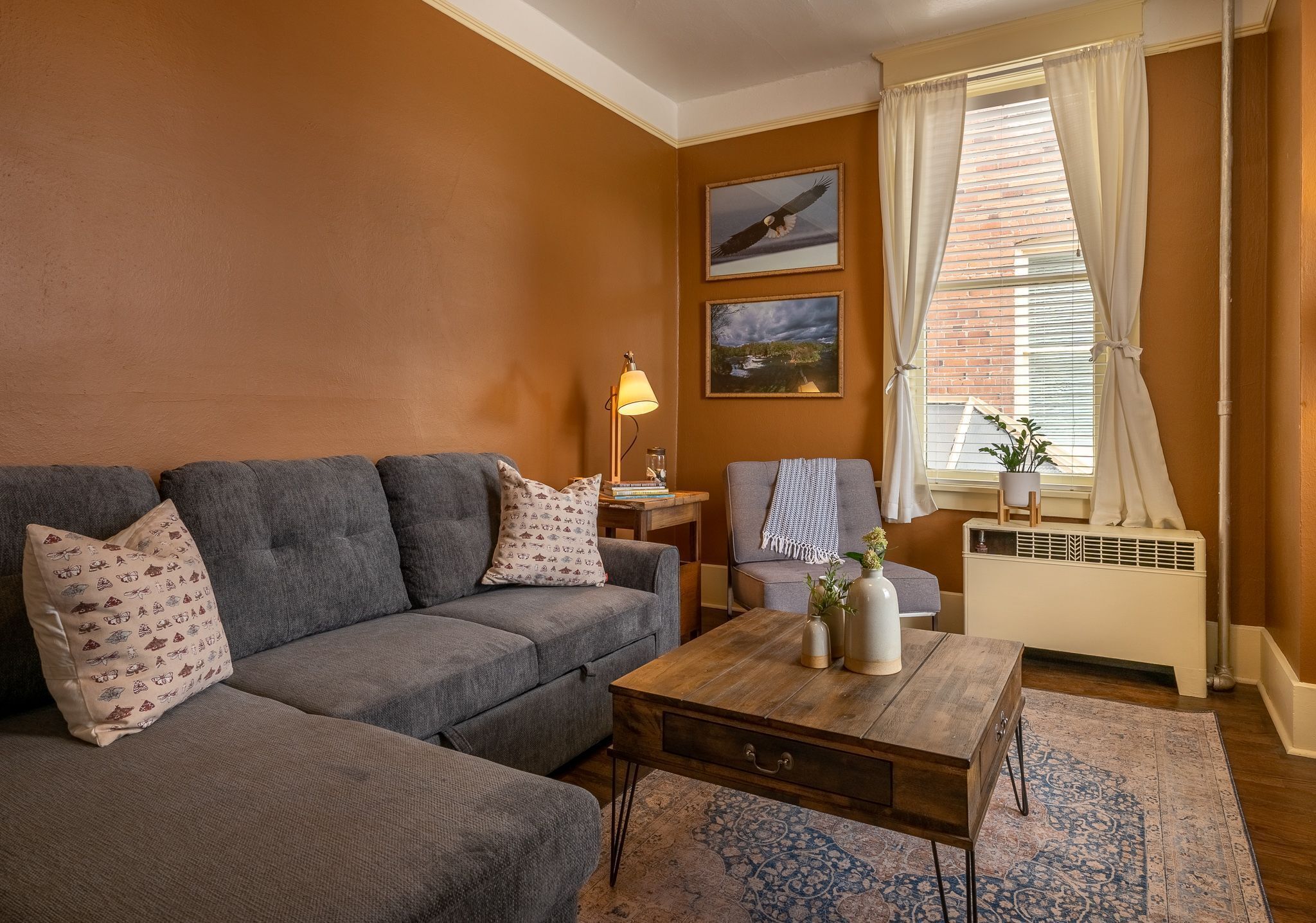 A living room with a grey sofa, a wooden coffee table, and a window with curtains.