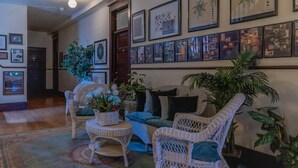 A hallway with wicker furniture, a patterned rug, and framed artwork on the wall.