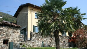 A stone building with a yellow facade, a palm tree in front, and a stone wall. - 2 1/2-room vacation apartment in Vercana, quiet and inviting above Lake Como (Vercana)
