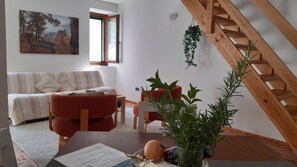 A living room with a sofa, a red chair, a wooden staircase, and a painting on the wall.