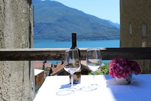 A table with a bottle and two glasses, a vase with flowers, and a scenic mountain view.