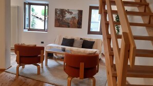 A living room with a sofa, two armchairs, a coffee table, and a wooden staircase. - 2 1/2-room vacation apartment in Vercana, quiet and inviting above Lake Como (Vercana)